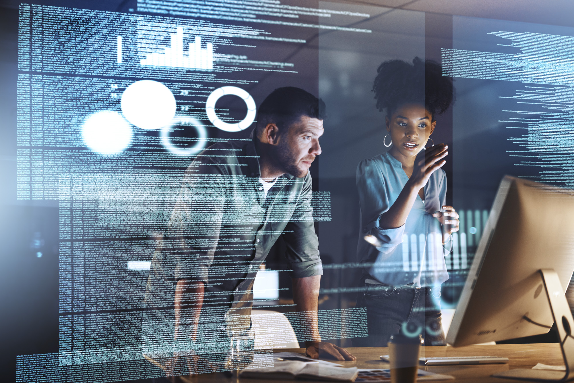 Two people collaborating in front of a screen with code and data showing.