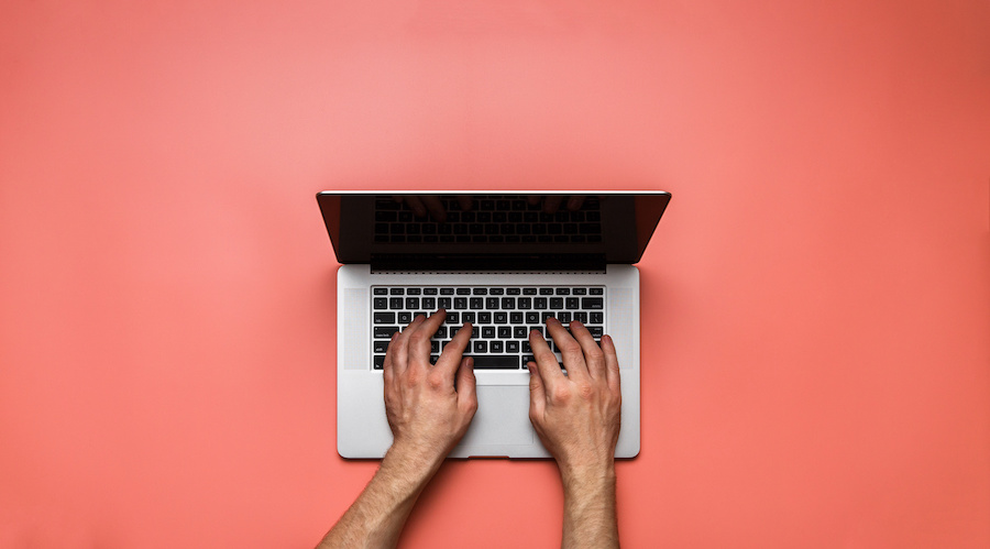 Someone typing on computer flatlay against red background