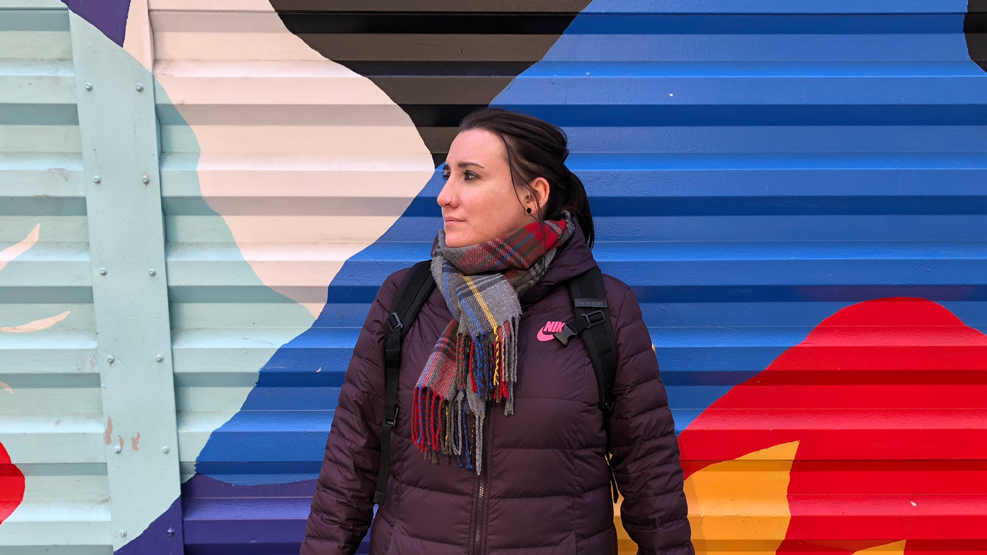 Angela Roche stood in front of colourful street art in New York. It&#39;s November and she is wearing a duvet jacket and a scarf.