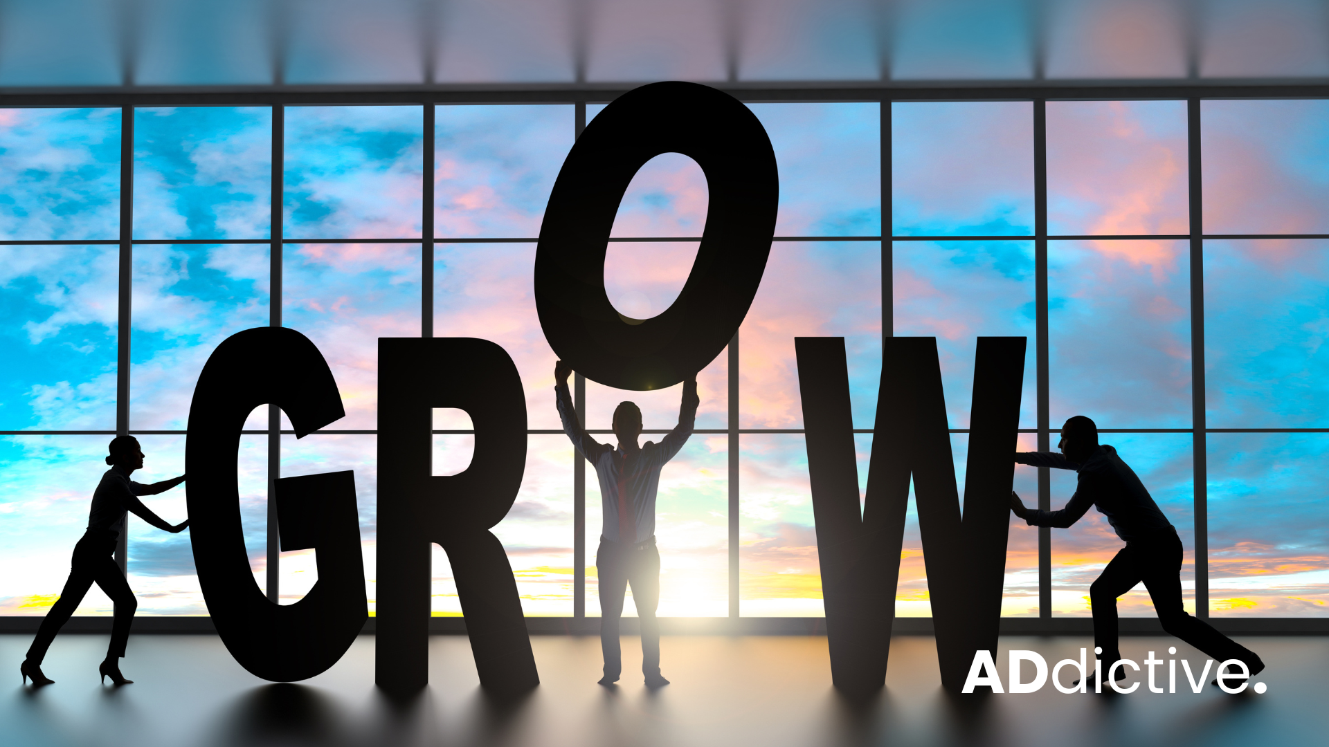 Siluette of business people holding letters to spell the word grow infront of a large window.