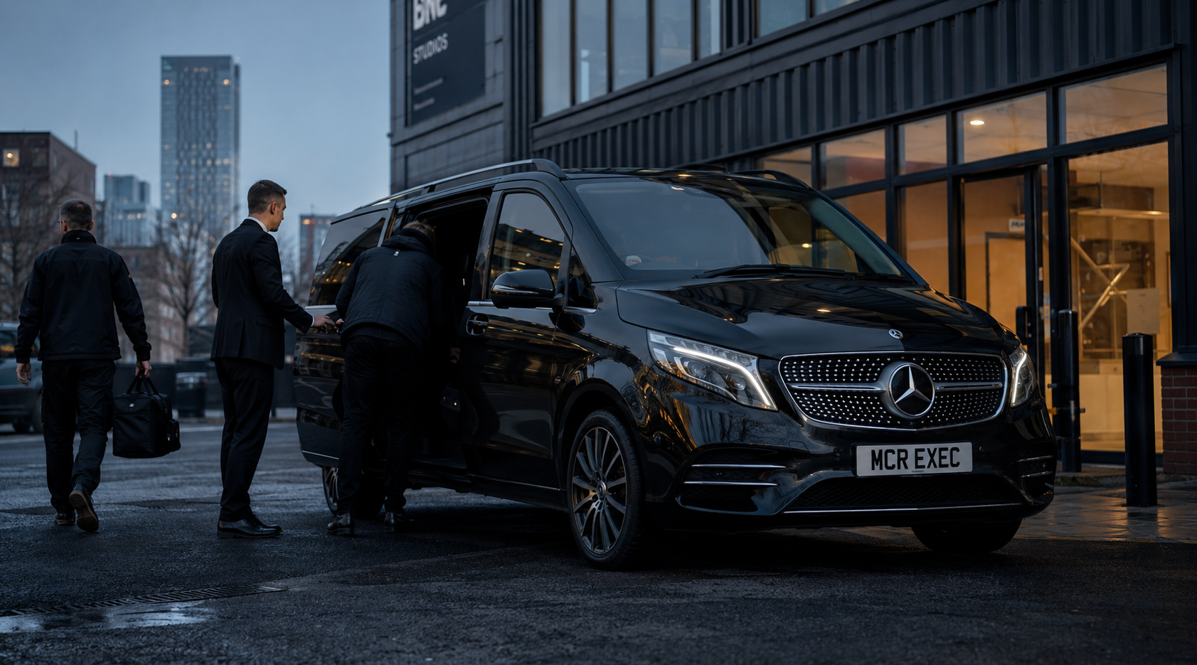 Black Mercedes V-Class chauffeur vehicle with MCR EXEC number plate outside a Manchester production facility, supporting film and TV production transport for crew, talent and media teams.