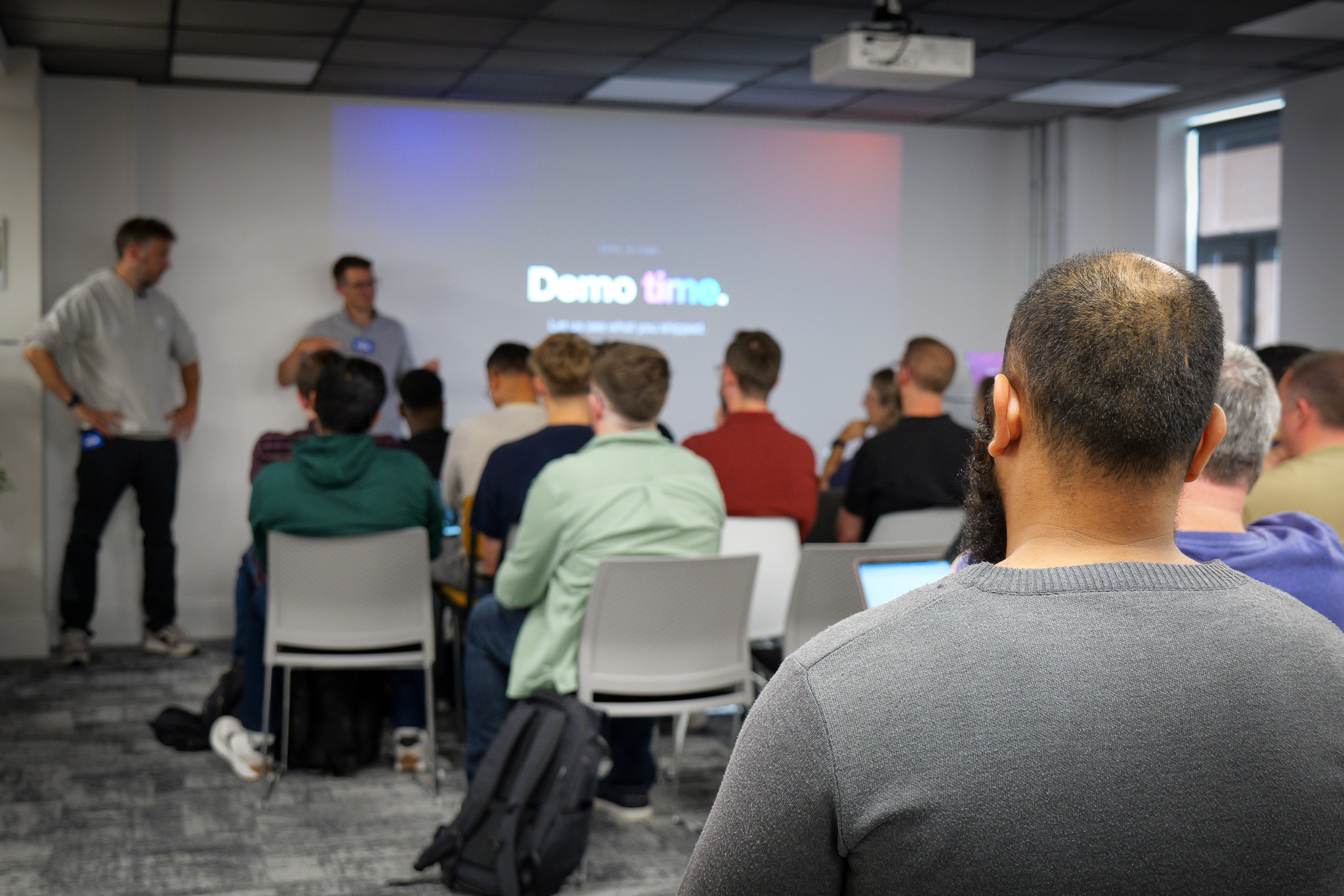 Group of people looking at a projector screen that reads 'Demo time'