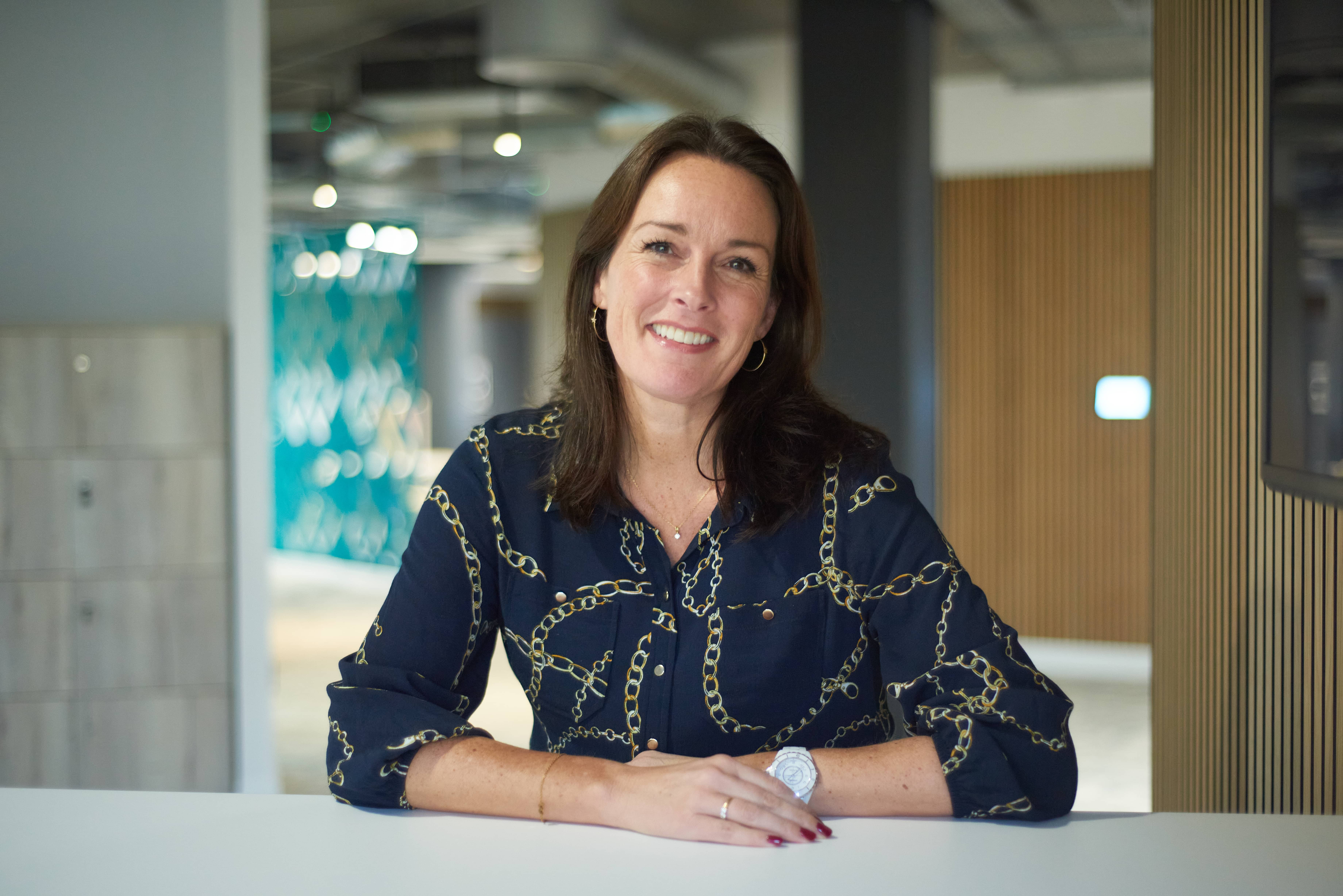 Pulsant's Wendy Shearer sits at a desk in a modern office. She is wearing a dark patterned blouse.