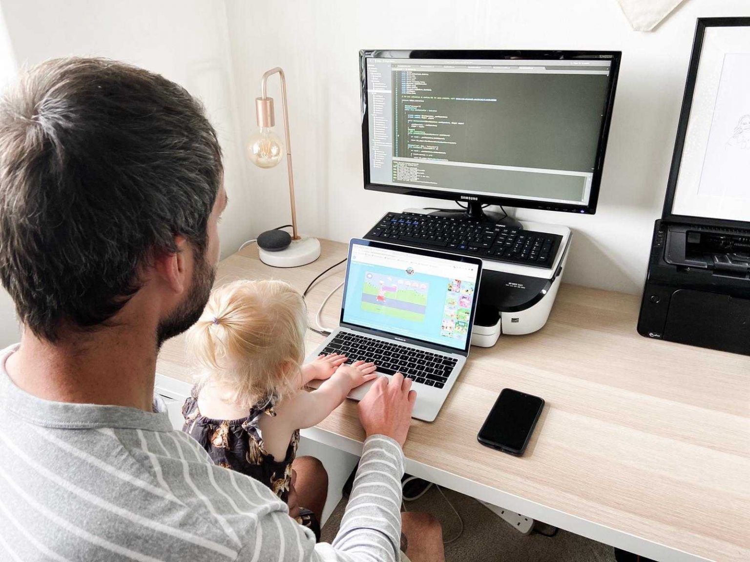 Father working at desktop with child sitting on his lap watching cartoons