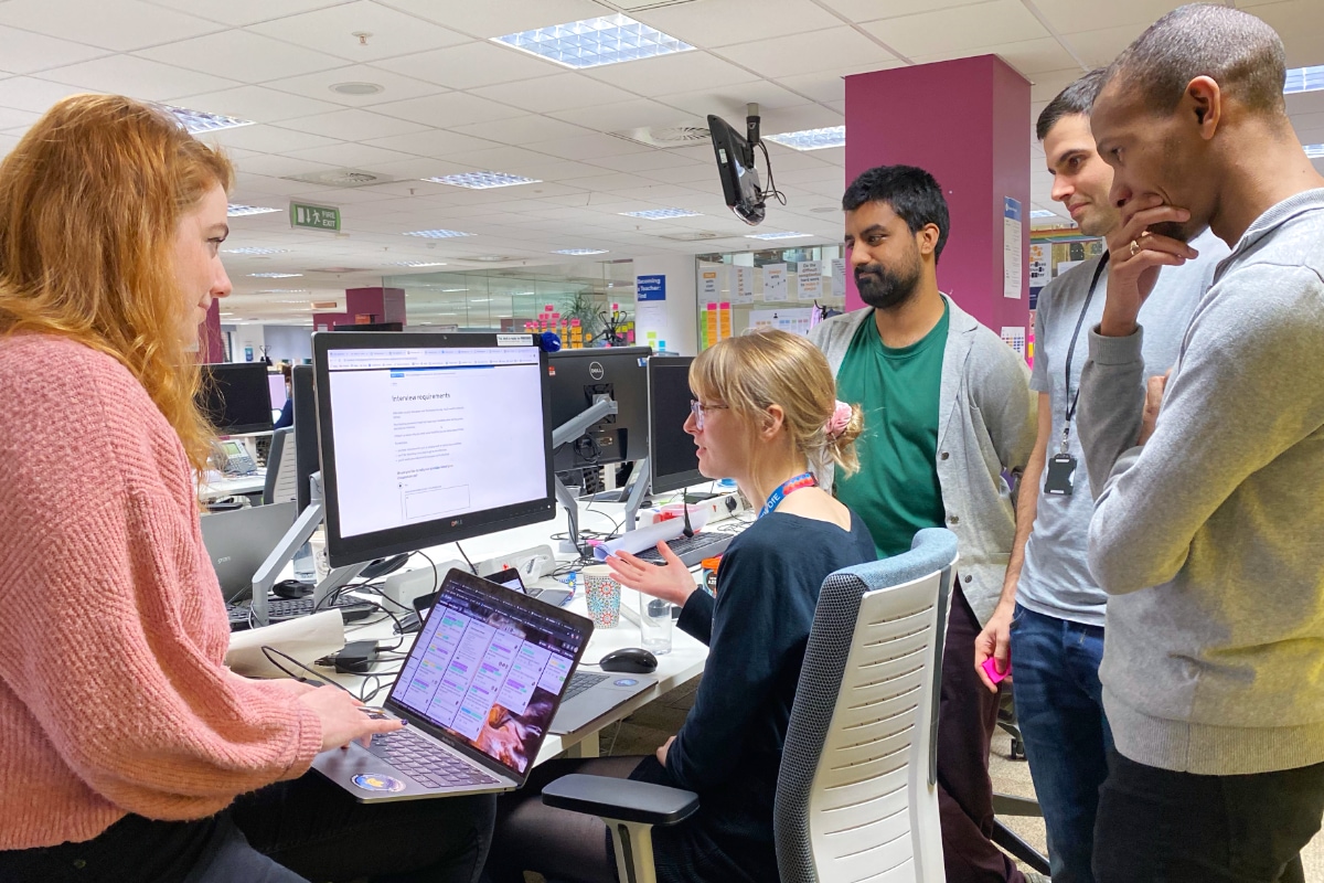 A group of colleagues gathered around a desktop in discussion